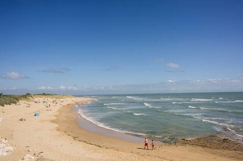 Escena de playa en Huttopia Côte Sauvage, un parque vacacional en Nouvelle-Aquitaine, Francia, con cielo azul.