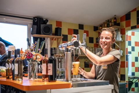 Una camarera sonriente sirve cerveza de barril en el bar de Huttopia Côte Sauvage en Nouvelle-Aquitaine, Francia.