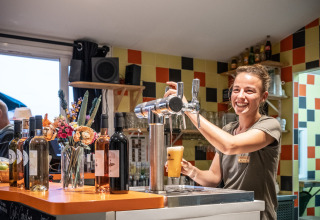 En smilende bartender tapper øl ved en bar på Huttopia Côte Sauvage feriepark i Nouvelle-Aquitaine, Frankrig.