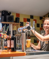 Eine lächelnde Barkeeperin schenkt Bier an der Bar im Huttopia Côte Sauvage in Nouvelle-Aquitaine, Frankreich aus.