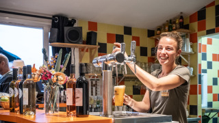A smiling bartender pours draft beer at the bar in Huttopia Côte Sauvage holiday park in Nouvelle-Aquitaine, France.