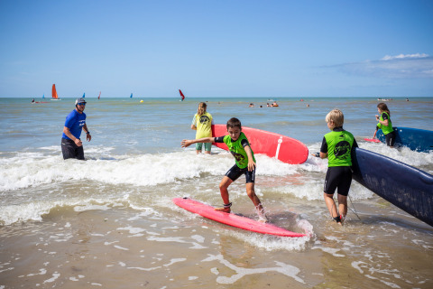 Niños aprenden a surfear con un instructor en la playa de Huttopia Côte Sauvage en Nouvelle-Aquitaine, Francia.