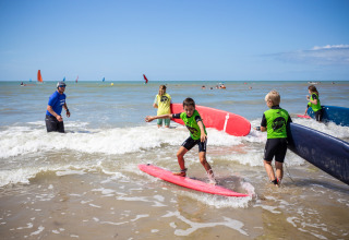 Børn lærer at surfe med instruktør på stranden ved Huttopia Côte Sauvage i Nouvelle-Aquitaine, Frankrig.