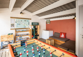 Indoor lounge area at Huttopia Côte Sauvage with foosball table, sofa, map, and information brochures.