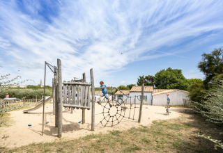 Børn leger på en naturlegeplads med klatrestativ i sandet på ferieparken Huttopia Côte Sauvage i Frankrig.