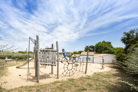 Niños jugando en un parque infantil de madera con arena y red para escalar en Huttopia Côte Sauvage, Francia.