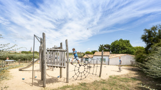 Children playing on a wooden playground with sand and climbing net at Huttopia Côte Sauvage holiday park, France.