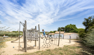 Kinder spielen auf einem Naturspielplatz mit Kletternetz im Ferienpark Huttopia Côte Sauvage in Frankreich.