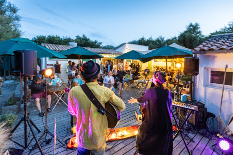 Concierto de música en vivo al aire libre al anochecer en Huttopia Côte Sauvage, Francia, con público atento.