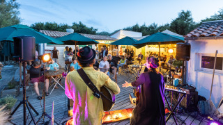 Outdoor evening live music performance on a deck at Huttopia Côte Sauvage, France, with an attentive audience.