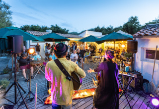Concierto de música en vivo al aire libre al anochecer en Huttopia Côte Sauvage, Francia, con público atento.