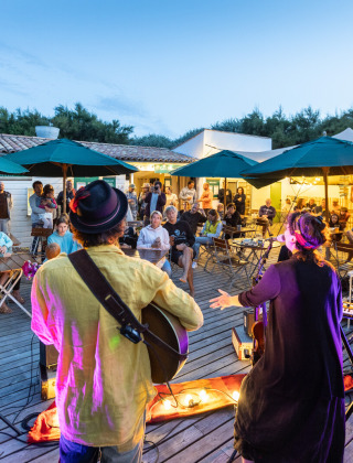 Abendliche Live-Musikperformance auf einer Terrasse im Huttopia Côte Sauvage, Frankreich, mit Zuschauern.