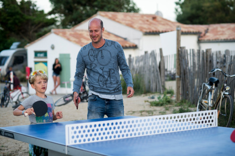 Un hombre y un niño juegan al tenis de mesa al aire libre en Huttopia Côte Sauvage, Nueva Aquitania, Francia.