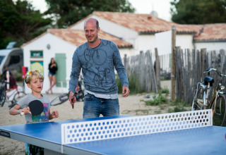 En mand og et barn spiller bordtennis udendørs i ferielandsbyen Huttopia Côte Sauvage i Frankrig.
