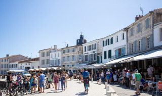 People stroll and relax on a sunny street lined with cafes in Sainte-Marie-de-Ré, Nouvelle-Aquitaine, France.