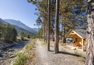 En hyggelig træhytte ved floden omgivet af fyrretræer i ferieparken Huttopia la Clarée, Provence-Alpes-Côte d’Azur.
