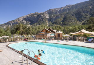 Udendørs swimmingpool på Huttopia la Clarée med børn der leger, omgivet af bjerge og skov i Frankrig.