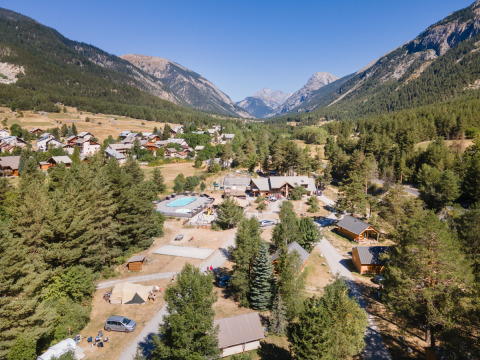Vista aérea del parque vacacional Huttopia la Clarée en Provenza-Alpes-Costa Azul rodeado de montañas y bosques.