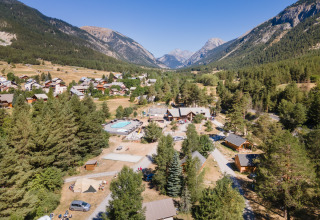 Vue aérienne du parc de vacances Huttopia la Clarée en Provence-Alpes-Côte d’Azur entouré de montagnes boisées.