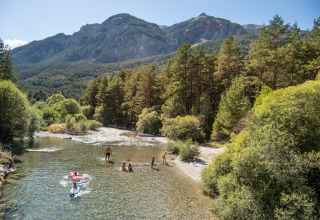 Urlauber baden in einem Fluss mit Blick auf Berge und Wälder bei Huttopia la Clarée in Frankreich.