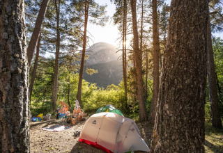 Campingplads i skov omgivet af bjerge i Provence-Alpes-Côte d’Azur, Frankrig, med telte og sollys.