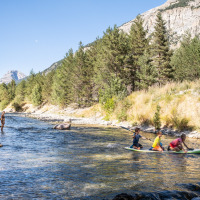 Niños juegan en una tabla de paddle en un río cerca de Val-Des-Près, rodeados de árboles y montañas.