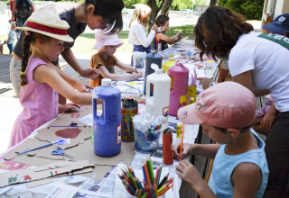 Enfants et adultes font des activités manuelles sur une table extérieure au parc de vacances Huttopia la Clarée, France.