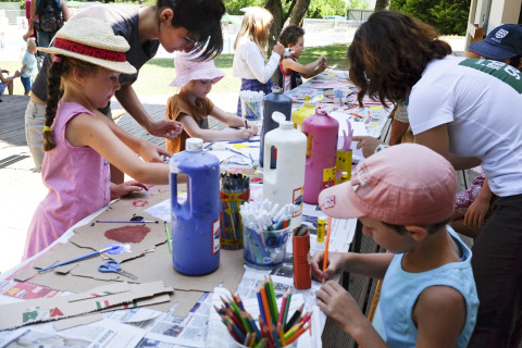 Children and adults doing arts and crafts at an outdoor table in Huttopia la Clarée holiday park, France.