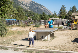 Un adulto e un bambino giocano a ping pong all'aperto a Huttopia la Clarée, con le montagne sullo sfondo.