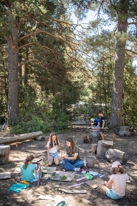 Niños haciendo manualidades al aire libre bajo altos árboles en Huttopia la Clarée, Provenza-Alpes-Costa Azul, Francia.