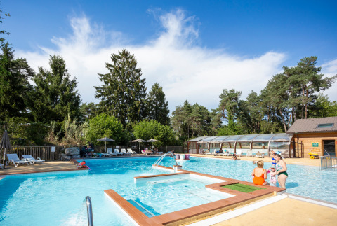 Udendørs swimmingpool med solbadende gæster og grøn skov i baggrunden på Camping La Pinède - Excenevex.