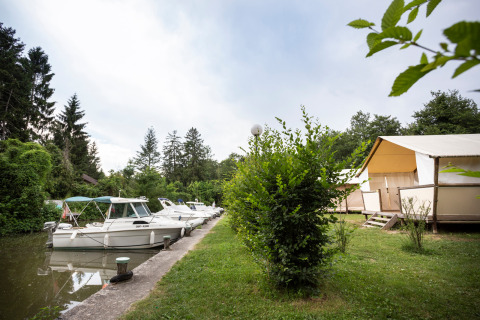 Bateaux amarrés sur un canal à côté de tentes lodges dans un parc de vacances verdoyant en Auvergne-Rhône-Alpes.