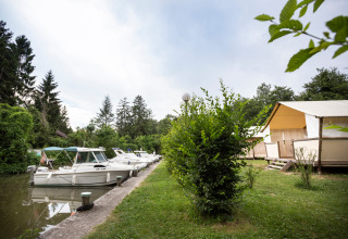 Boten afgemeerd aan een kanaal naast lodgetenten in een groene vakantiepark in Auvergne-Rhône-Alpes, Frankrijk.