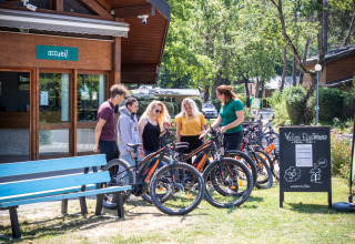 Bezoekers van Camping La Pinède in Excenevex krijgen uitleg over elektrische fietsen bij de receptie.