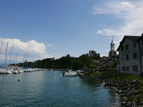 Hafenansicht bei Camping La Pinède - Excenevex mit Segelbooten, Kirche und traditionellen Häusern.
