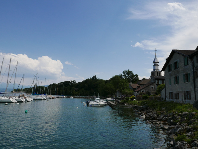 Harbor view at Camping La Pinède - Excenevex with sailboats, historic church, and scenic waterfront homes.