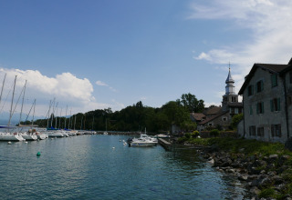 Vista sul porto al Camping La Pinède - Excenevex con barche a vela, chiesa e case sul lungolago.