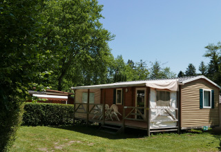 Stacaravan met terras en tuinmeubilair in een groene omgeving op Camping La Pinède, Excenevex, Frankrijk.