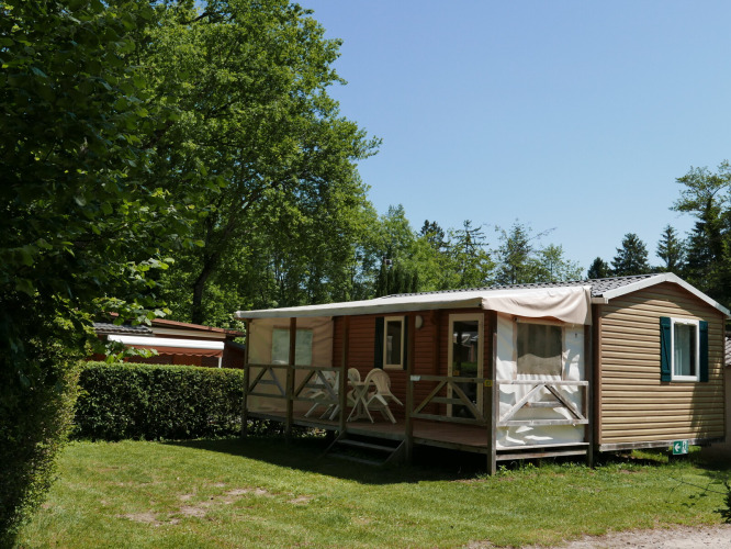 Mobile home with furnished porch surrounded by trees and greenery at Camping La Pinède, Excenevex, France.