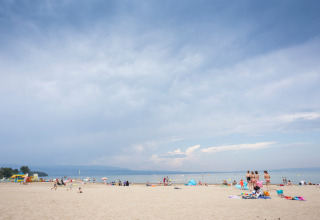 Beach scene at Camping La Pinède - Excenevex holiday park in Auvergne-Rhône-Alpes, France, with visitors.