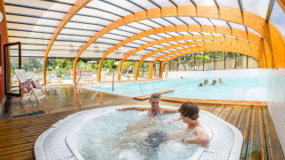 Piscina cubierta con jacuzzi y familias disfrutando en Camping La Pinède - Excenevex, Auvergne-Rhône-Alpes, Francia.