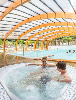 Piscina cubierta con jacuzzi y familias disfrutando en Camping La Pinède - Excenevex, Auvergne-Rhône-Alpes, Francia.
