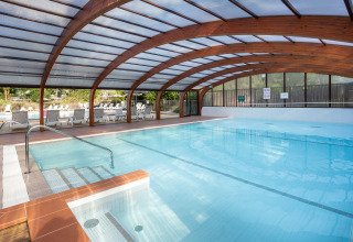 Überdachtes Schwimmbad mit Holzrahmen und Sonnenliegen im Ferienpark Camping La Pinède in Excenevex, Frankreich.