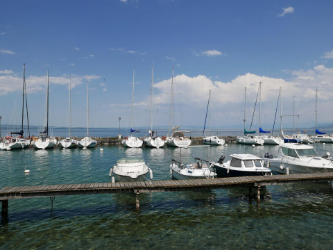 Veleros y barcos atracados en Camping La Pinède - Excenevex en Auvergne-Rhône-Alpes, Francia, con fondo azul.