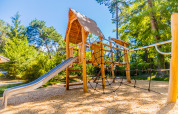 Parco giochi con scivolo e rete da arrampicata circondato da alberi al Camping La Pinède in Francia.