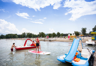 Scène de plage au Camping La Pinède - Excenevex avec pédalos, paddle et vacanciers dans l'eau.