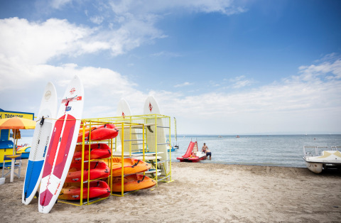 Kayaks y tablas de paddle surf en la playa de Excenevex-Plage, Francia, junto al lago, bajo un cielo azul.