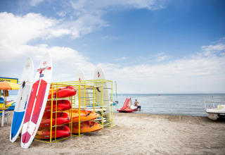 Kajaks en paddleboards aan het strand van Excenevex-Plage, Frankrijk, met kalm water en open hemel.