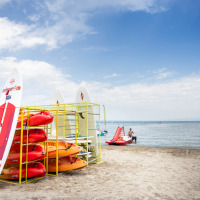 Kayaks y tablas de paddle surf en la playa de Excenevex-Plage, Francia, junto al lago, bajo un cielo azul.