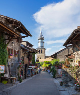 Calle antigua con flores en Excenevex-Plage, Auvergne-Rhône-Alpes, Francia, con una iglesia al fondo.